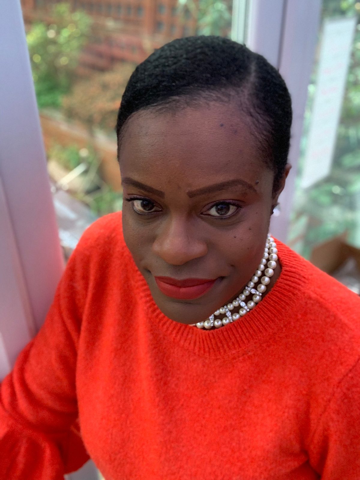 Joycellyn Akuffo smiling, in a red jumper and pearls